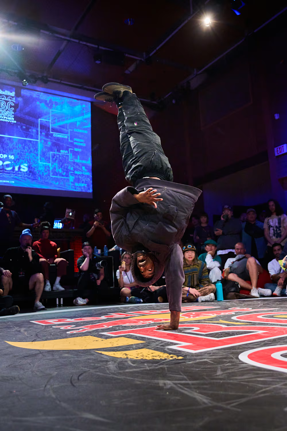B-Boy Sleepy exécutant un 1990 lors d’une compétition de breakdance Red Bull BC One devant un public.