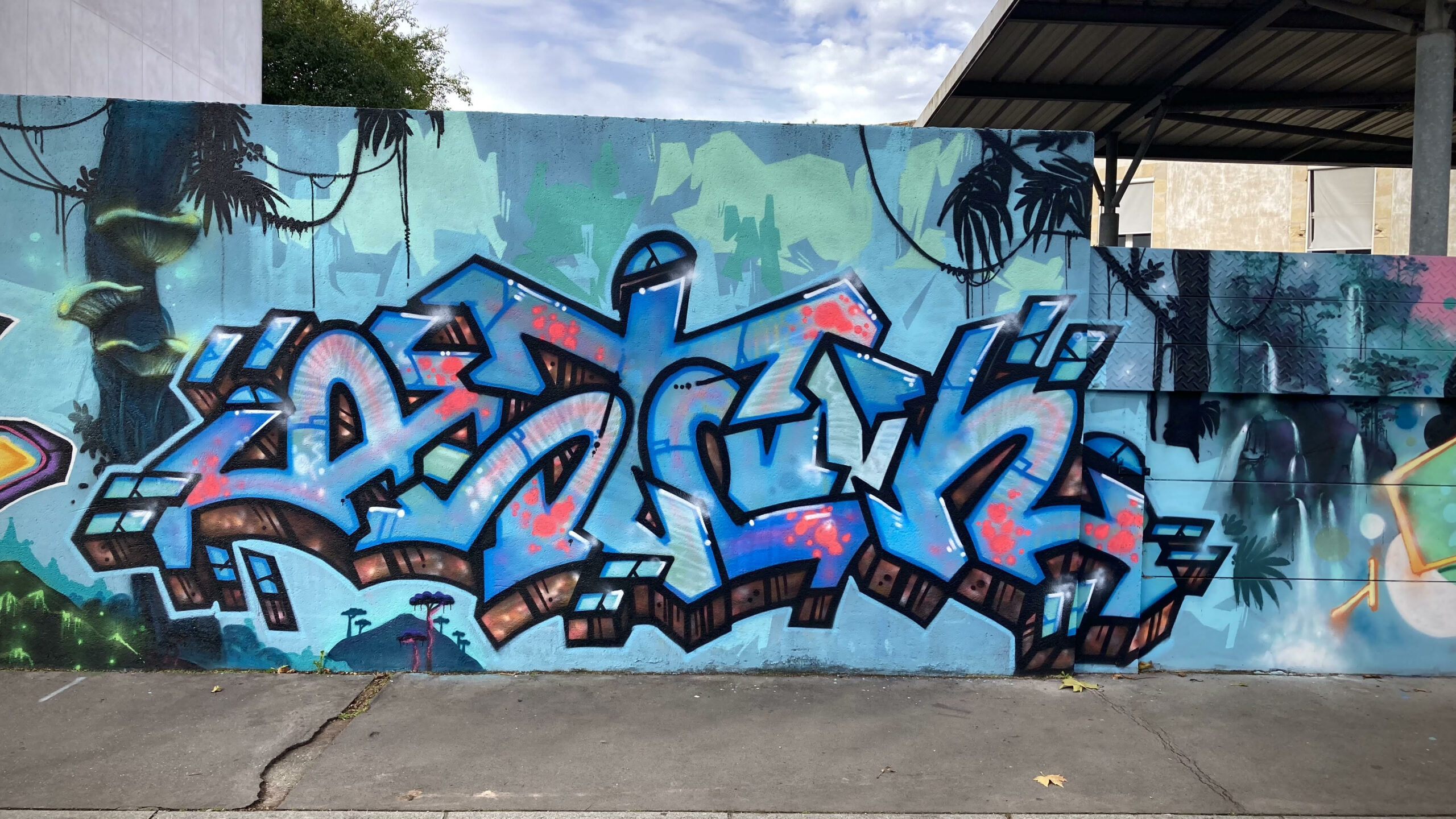 Fresque graffiti lettrage coloré bleu et rose réalisée lors de la JAM D’ARC 25 à Cenon, inspirée de l’univers Pandora Avatar, sur un mur extérieur.