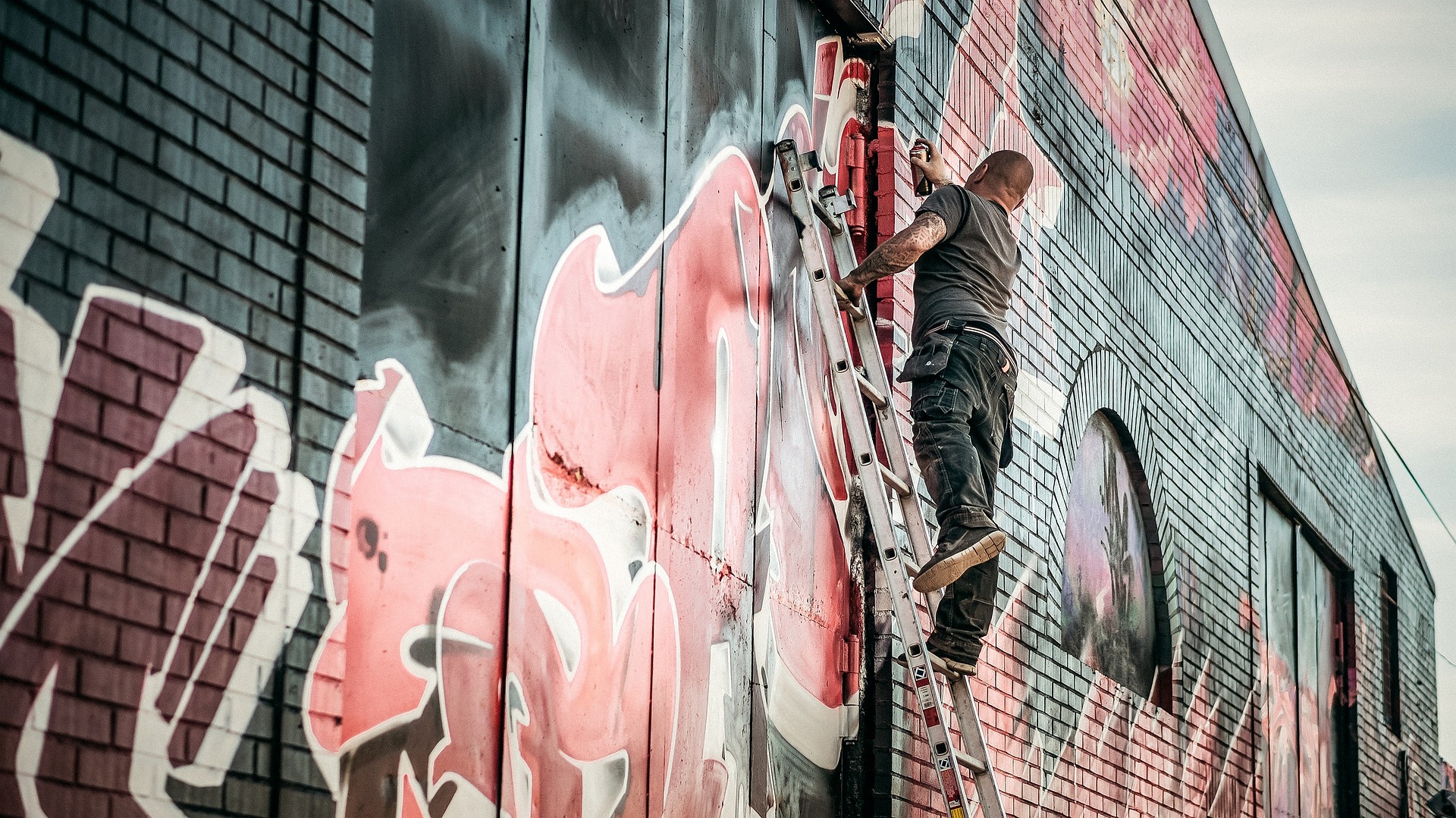Artiste graffiti réalisant une fresque murale sur un bâtiment à l’aide d’une échelle