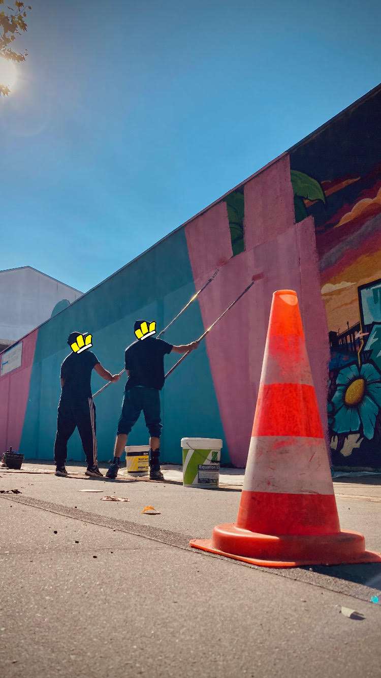 Artistes WOLS en train de peindre une fresque murale avec rouleaux sur un mur extérieur lors d’un projet de street art urbain