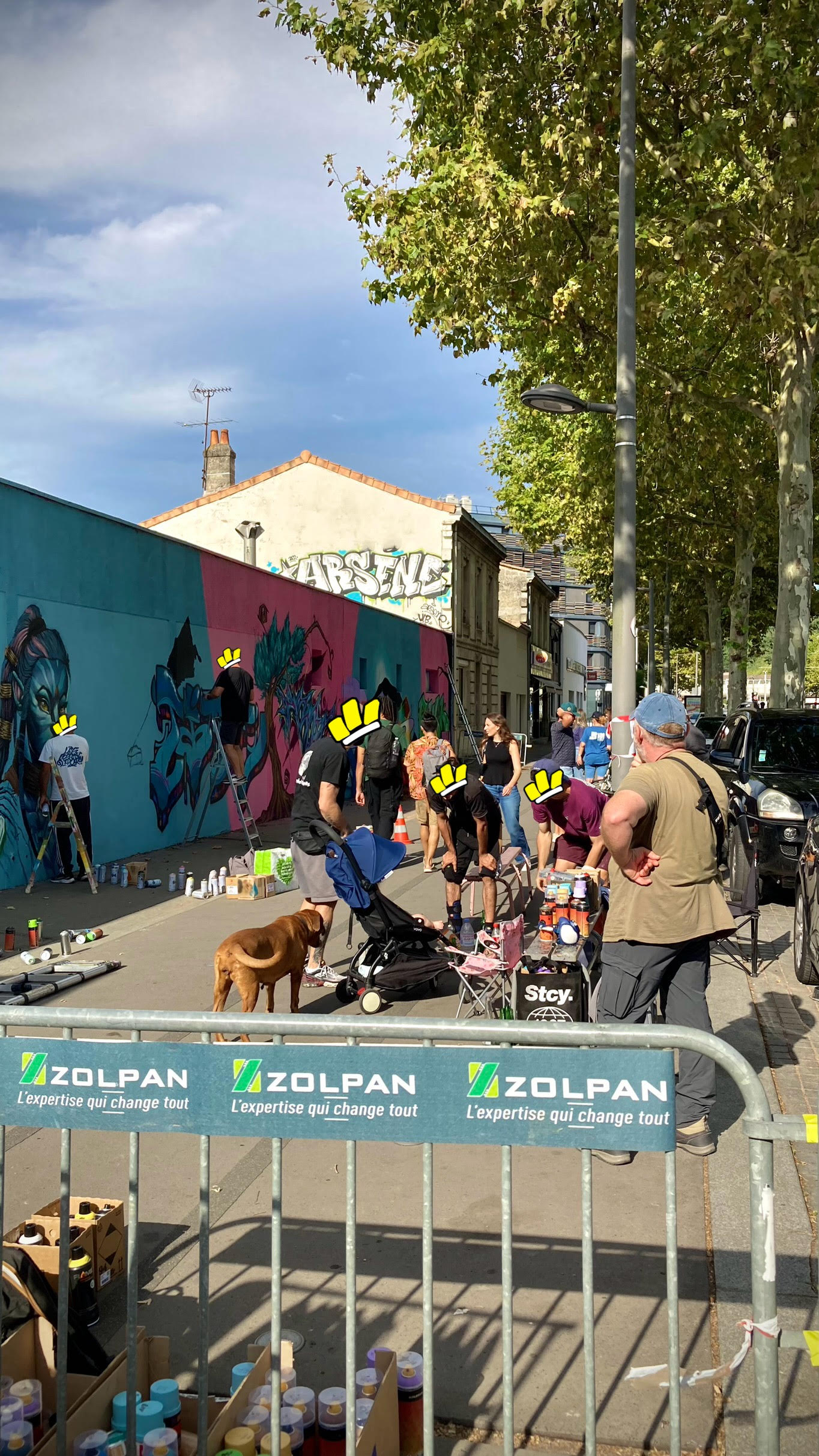 Vue d’ensemble d’un événement street art avec public, artistes et fresque murale en cours de réalisation