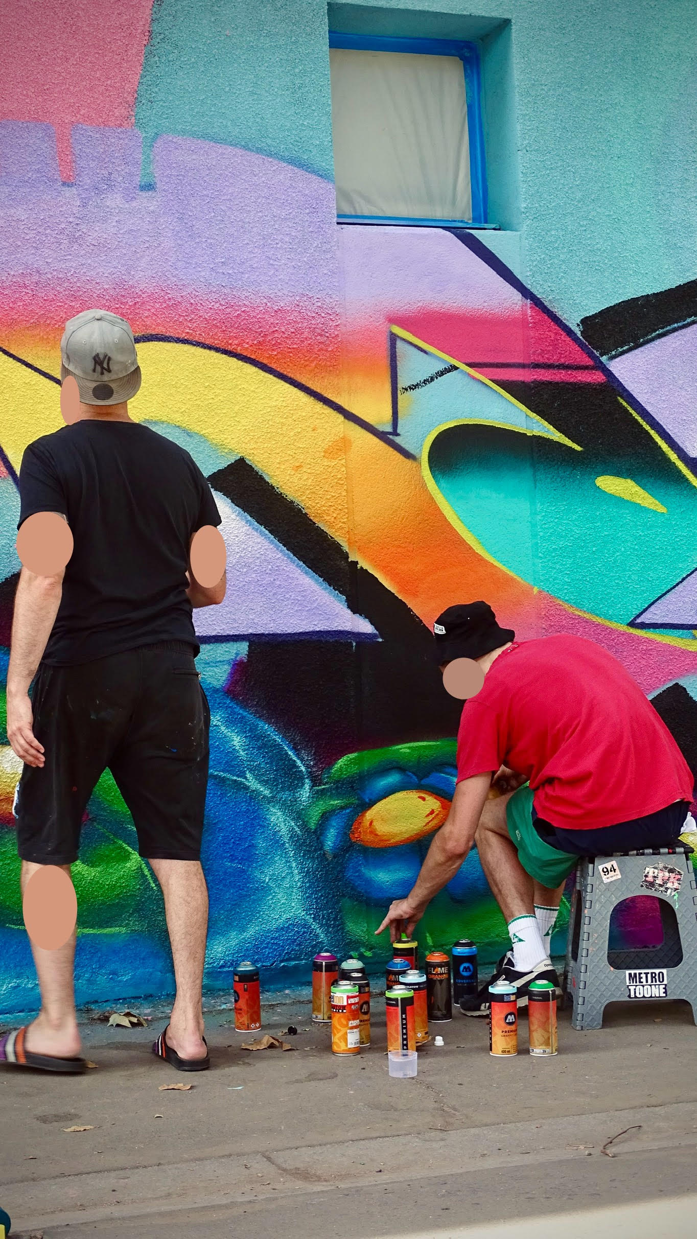 Artistes graffiti sélectionnant des bombes de peinture devant une fresque colorée en cours de réalisation