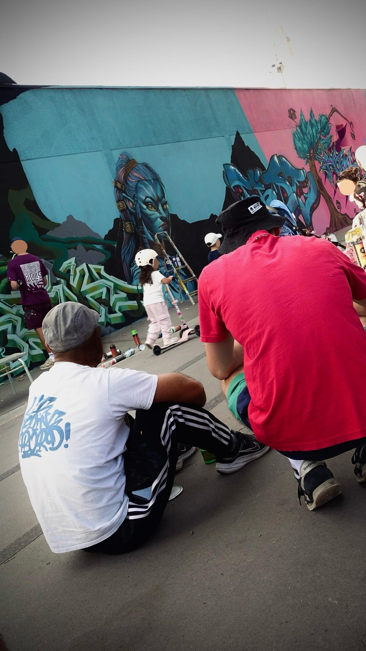 Public et artistes observant une fresque graffiti en cours avec ambiance conviviale