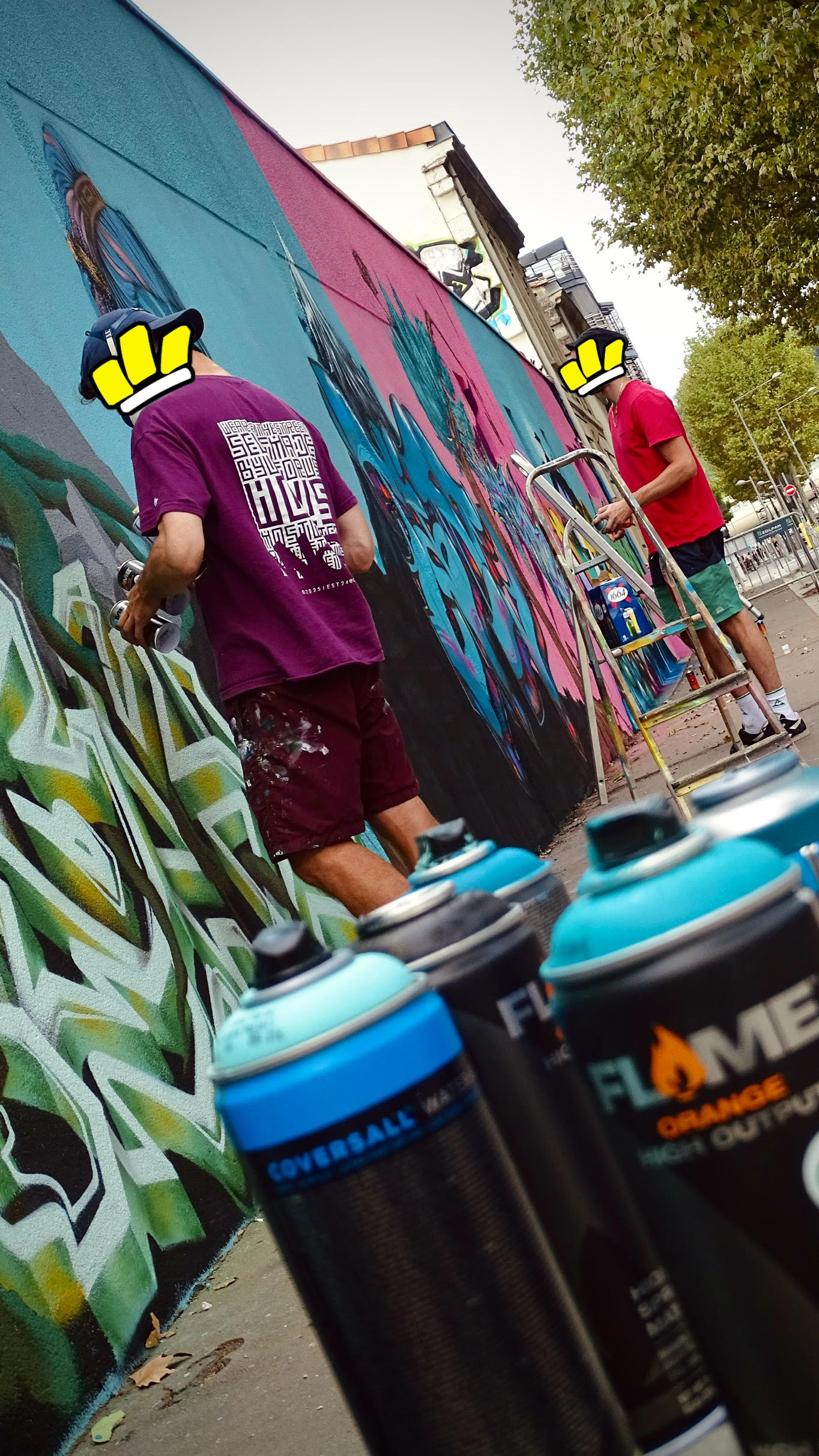 Bombes de peinture au premier plan avec artistes réalisant une fresque graffiti en arrière-plan