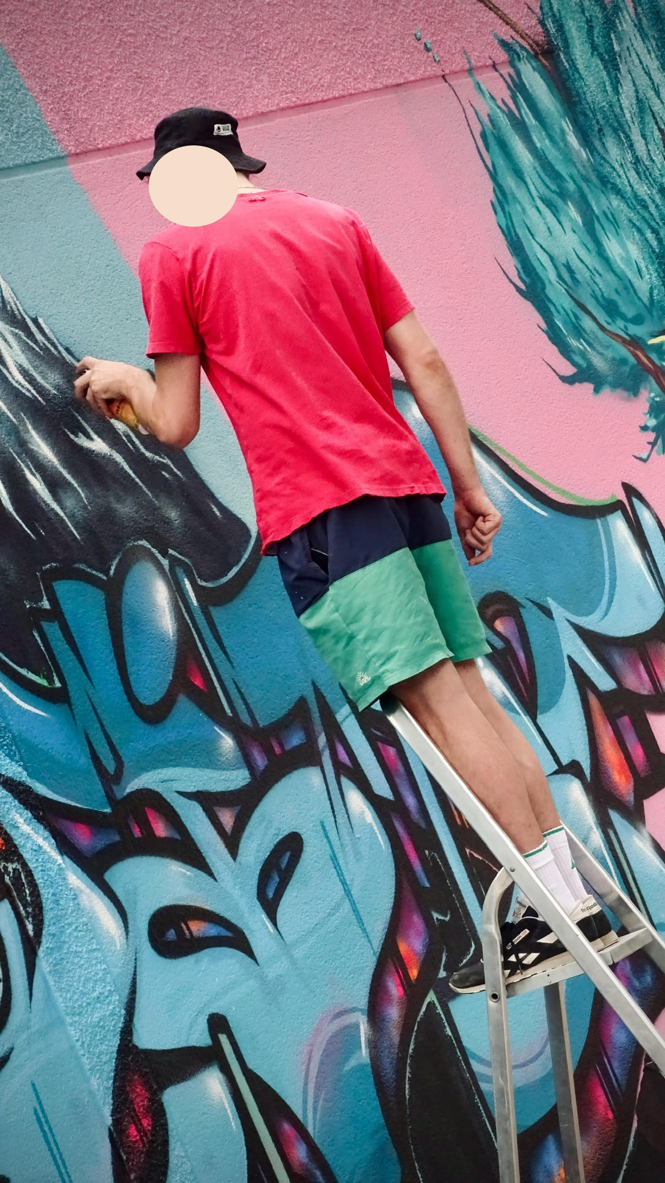 Artiste sur escabeau peignant des détails précis sur une fresque graffiti colorée