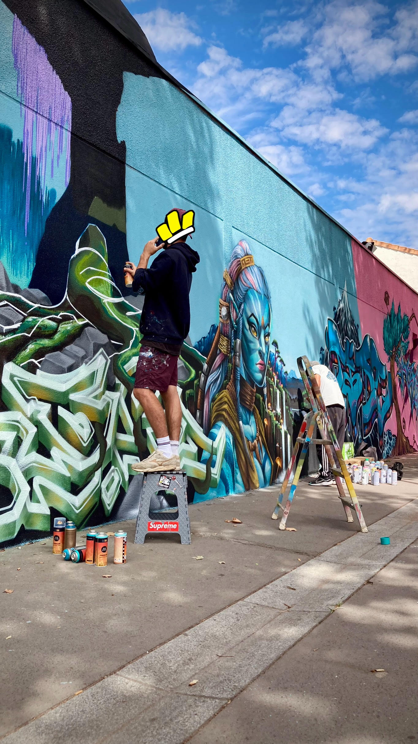 Artistes réalisant une fresque Avatar avec portrait et graffiti sur un mur extérieur