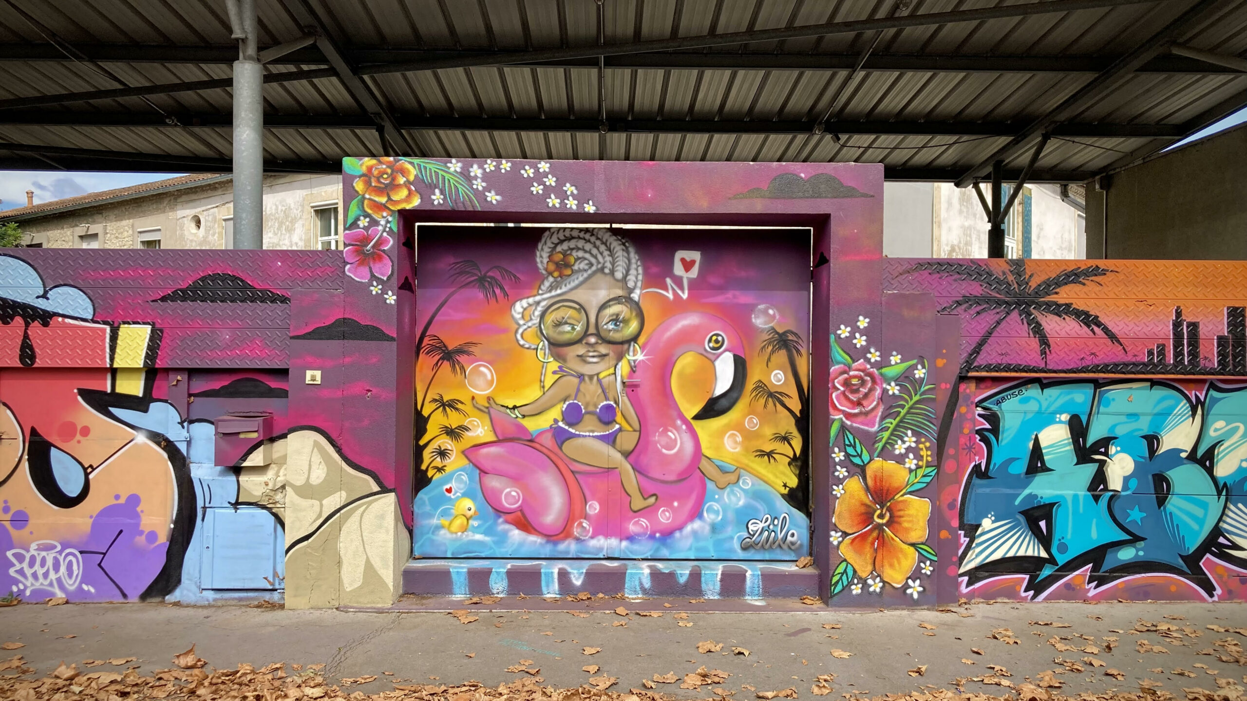 Personnage street art représentant une femme sur une bouée flamant rose dans un décor tropical.