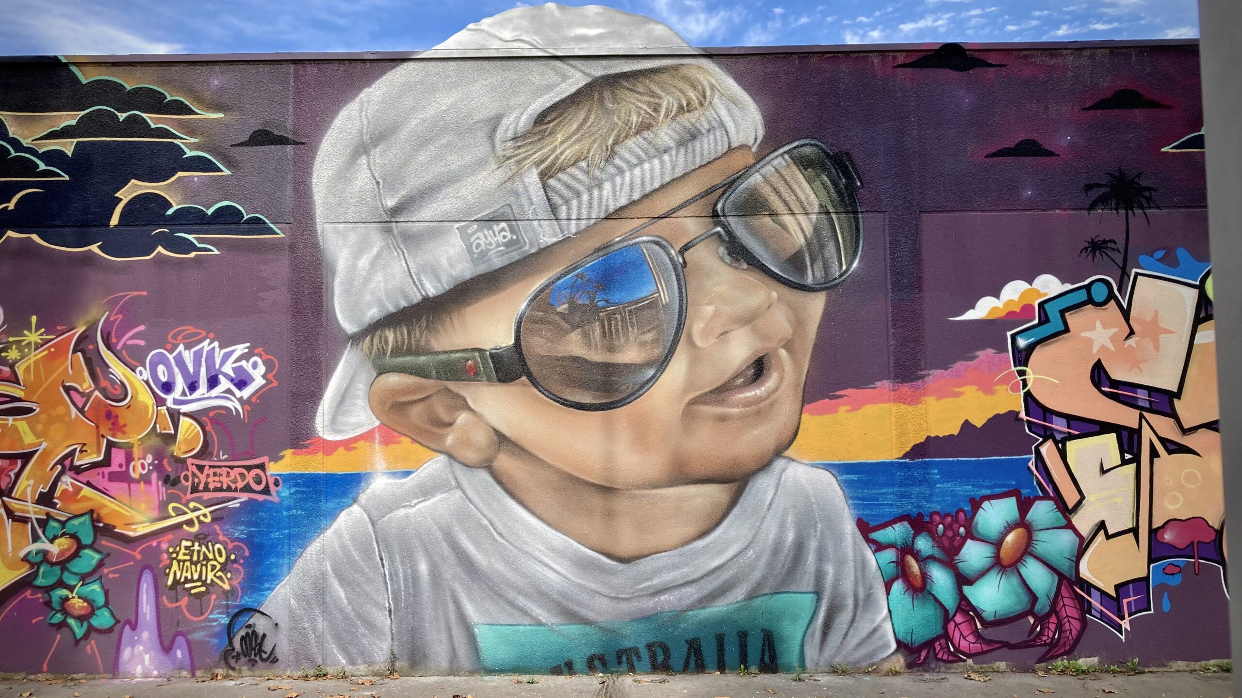 Portrait graffiti réaliste d’un enfant avec lunettes sur fond tropical.