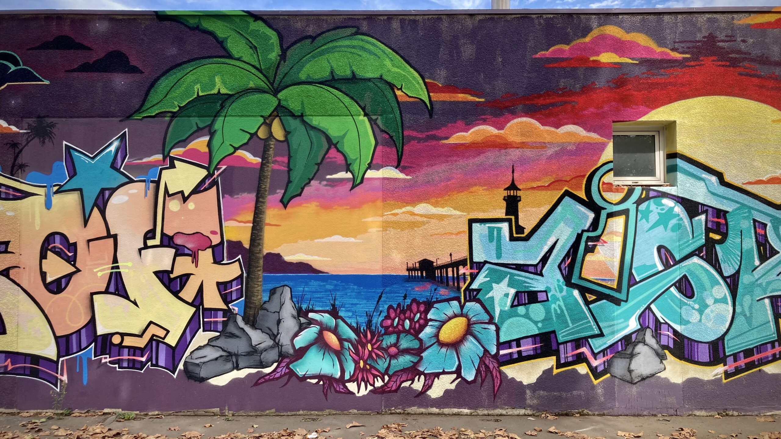 Fresque graffiti avec palmier, océan et lettrage coloré.