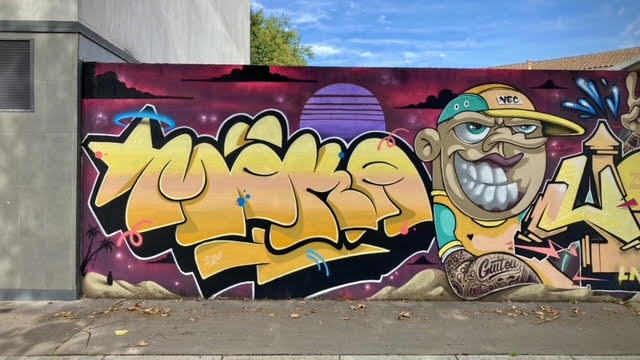 Fresque graffiti avec lettrage jaune et personnage cartoon réalisée à Cenon.