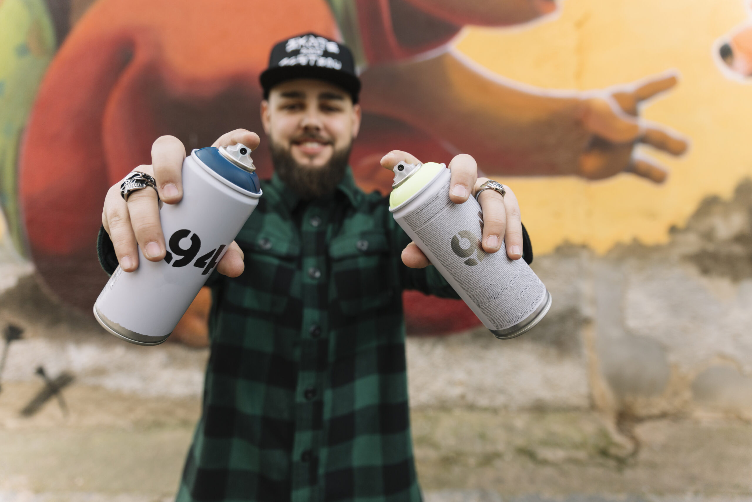Artiste graffiti présentant des bombes de peinture aérosol devant une fresque street art