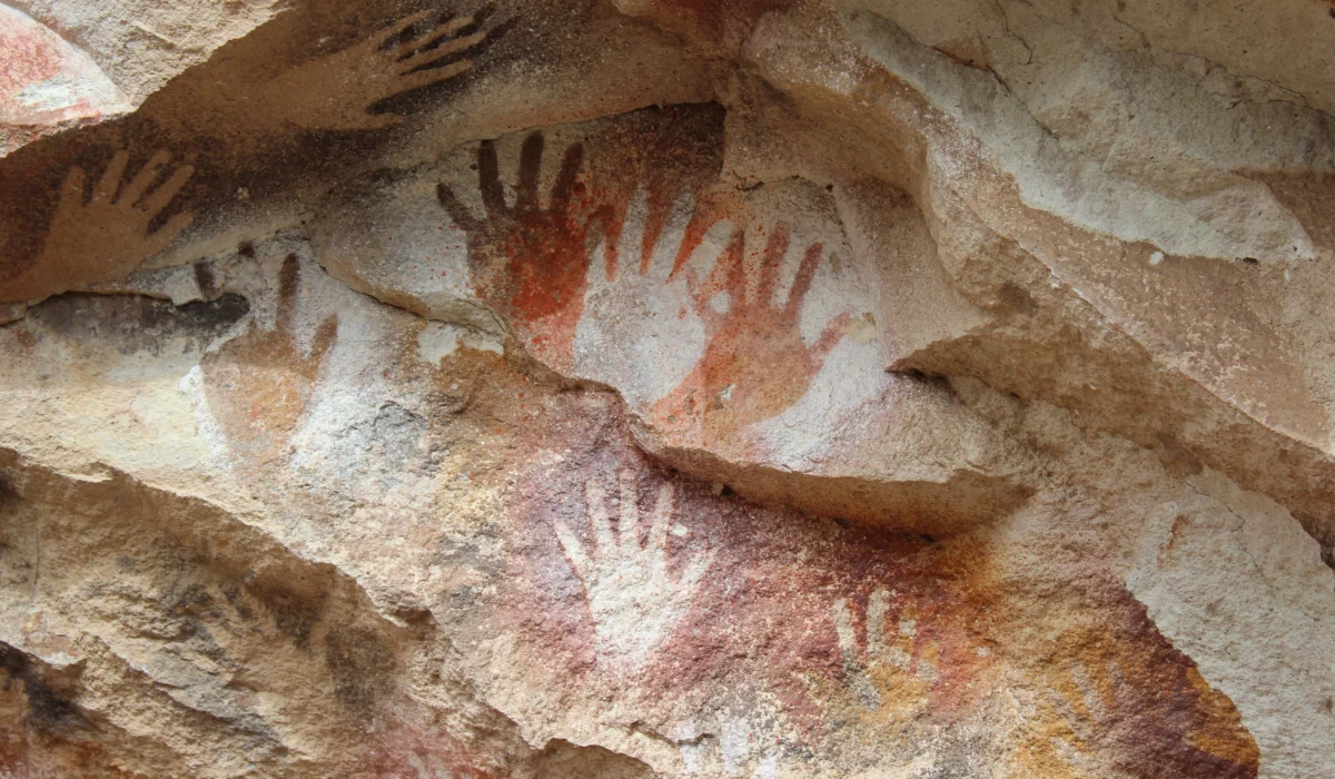 Empreintes de mains préhistoriques rouges et noires peintes sur les parois rocheuses d’une grotte.