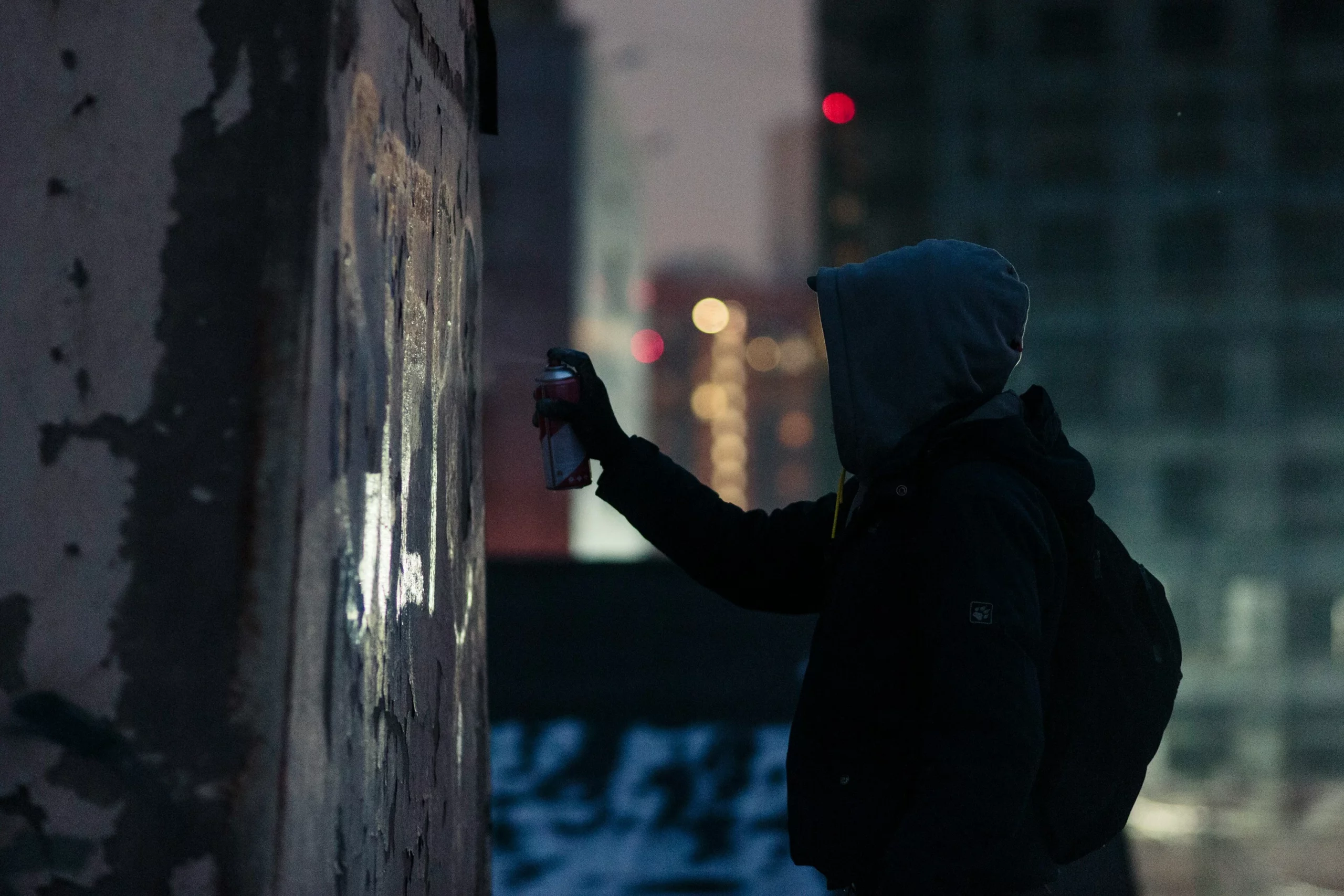 Graffeur encapuchonné réalisant un graffiti à la bombe de peinture sur un mur la nuit.