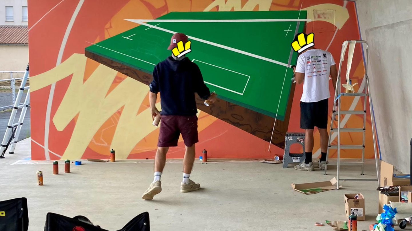 Artistes réalisant une fresque street art représentant un terrain multisport dans un équipement sportif à Floirac.