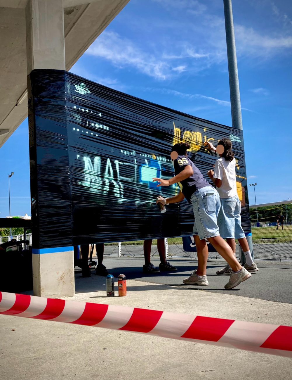 Deux participantes s’initient à la bombe de peinture sur un mur éphémère pendant l’atelier graffiti CAP33 à Floirac.