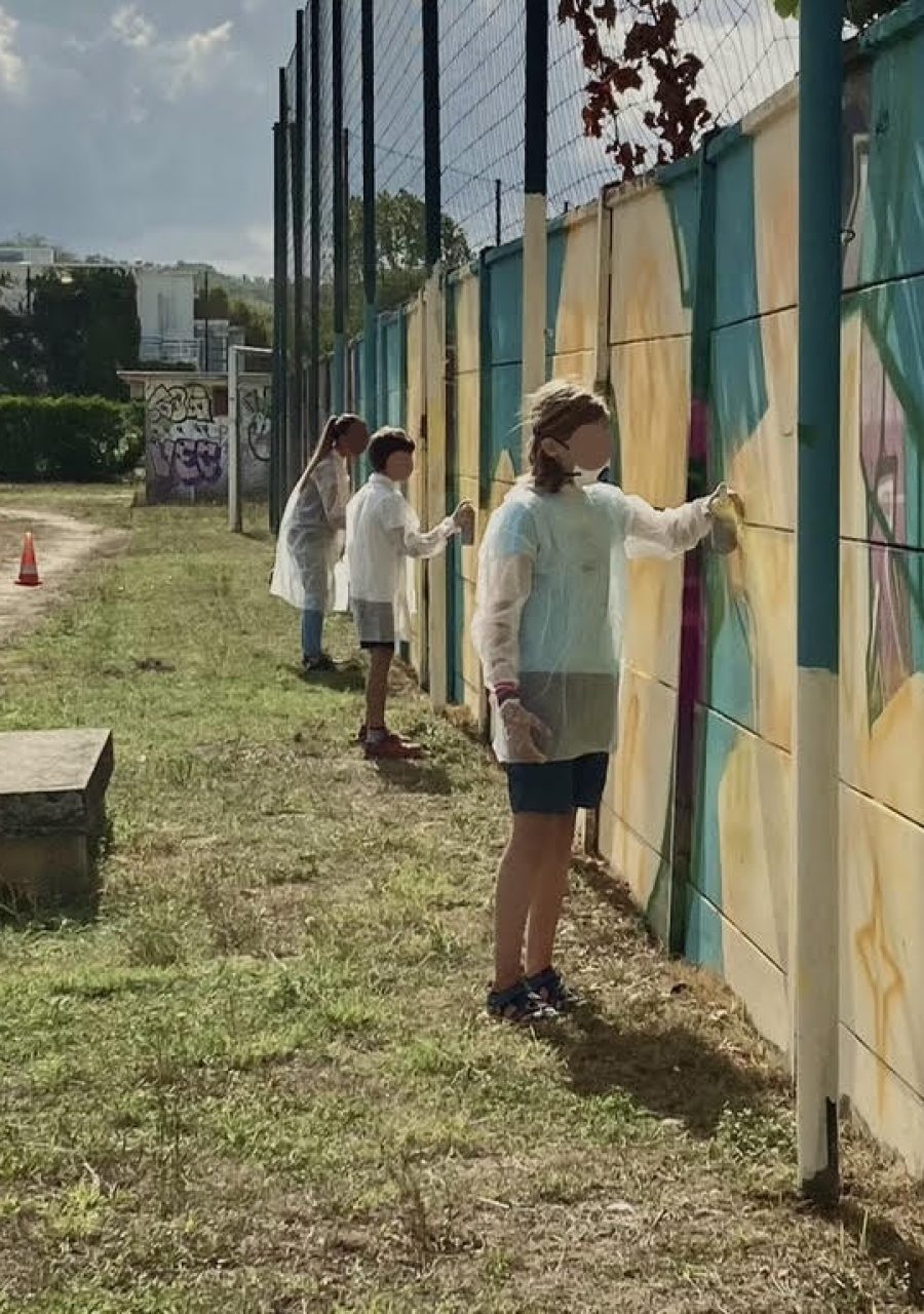 Participants peignant à la bombe le lettrage graffiti FLOIRAC lors d’une œuvre participative au stade Jean-Raymond Guyon à Floirac.