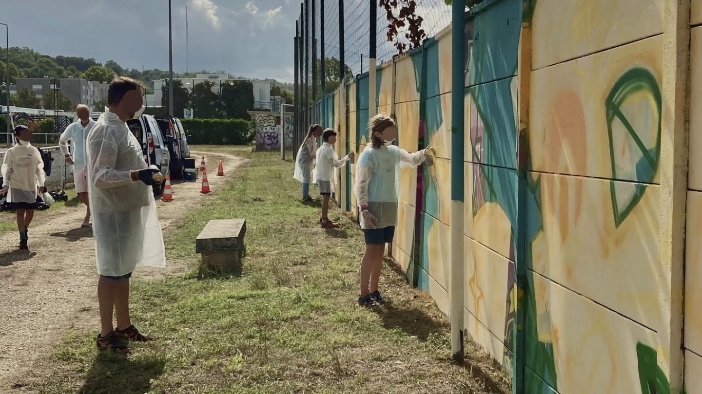 Participants peignant à la bombe le lettrage graffiti FLOIRAC lors d’une œuvre participative au stade Jean-Raymond Guyon à Floirac.