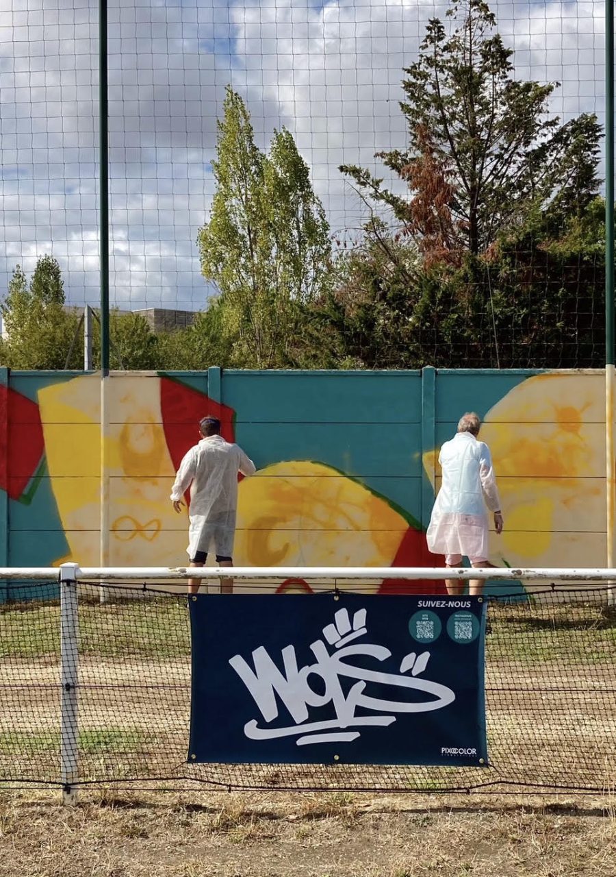 Vue d’ensemble de la fresque participative FLOIRAC avec plusieurs participants peignant le mur du stade Jean-Raymond Guyon à Floirac.