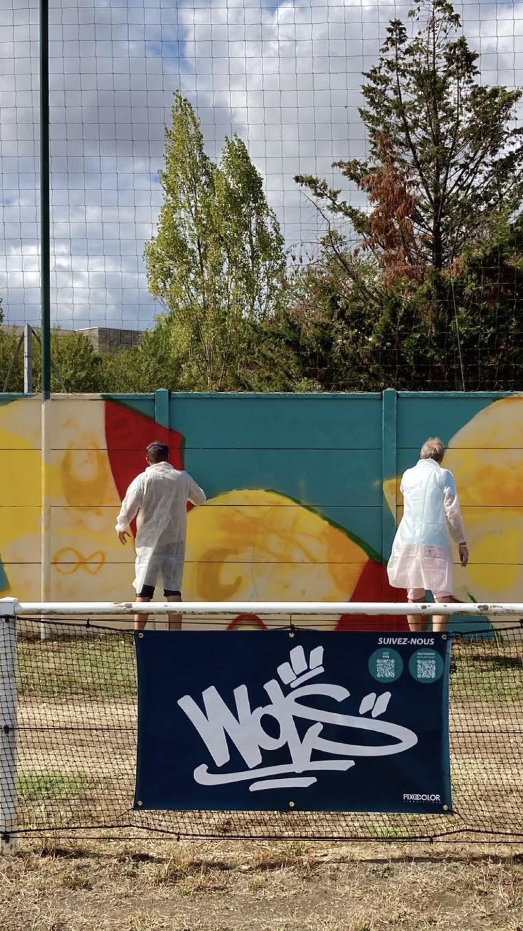 Vue d’ensemble de la fresque participative FLOIRAC avec plusieurs participants peignant le mur du stade Jean-Raymond Guyon à Floirac.