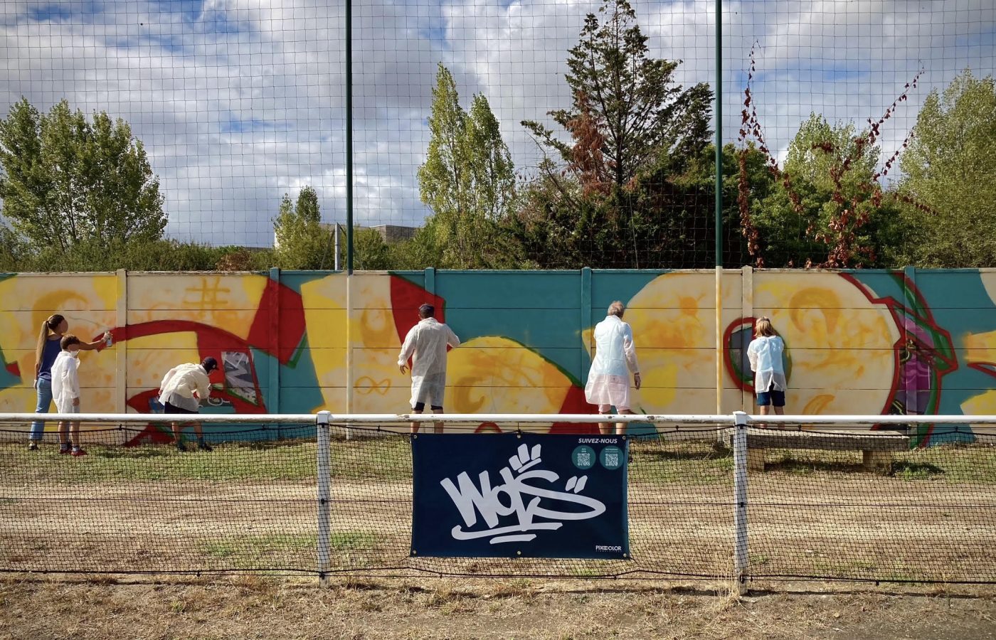 Vue d’ensemble de la fresque participative FLOIRAC avec plusieurs participants peignant le mur du stade Jean-Raymond Guyon à Floirac.
