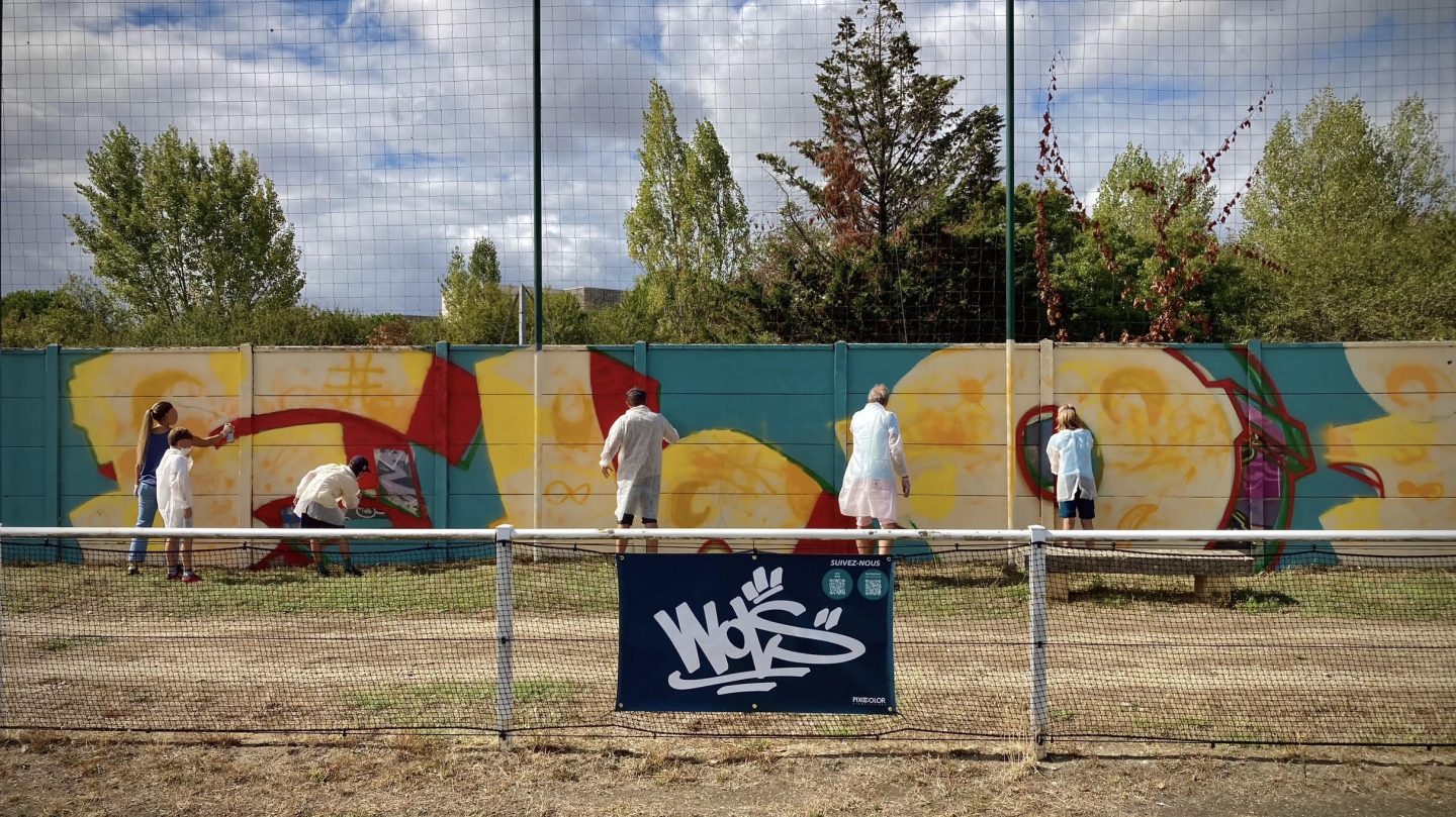 Vue d’ensemble de la fresque participative FLOIRAC avec plusieurs participants peignant le mur du stade Jean-Raymond Guyon à Floirac.