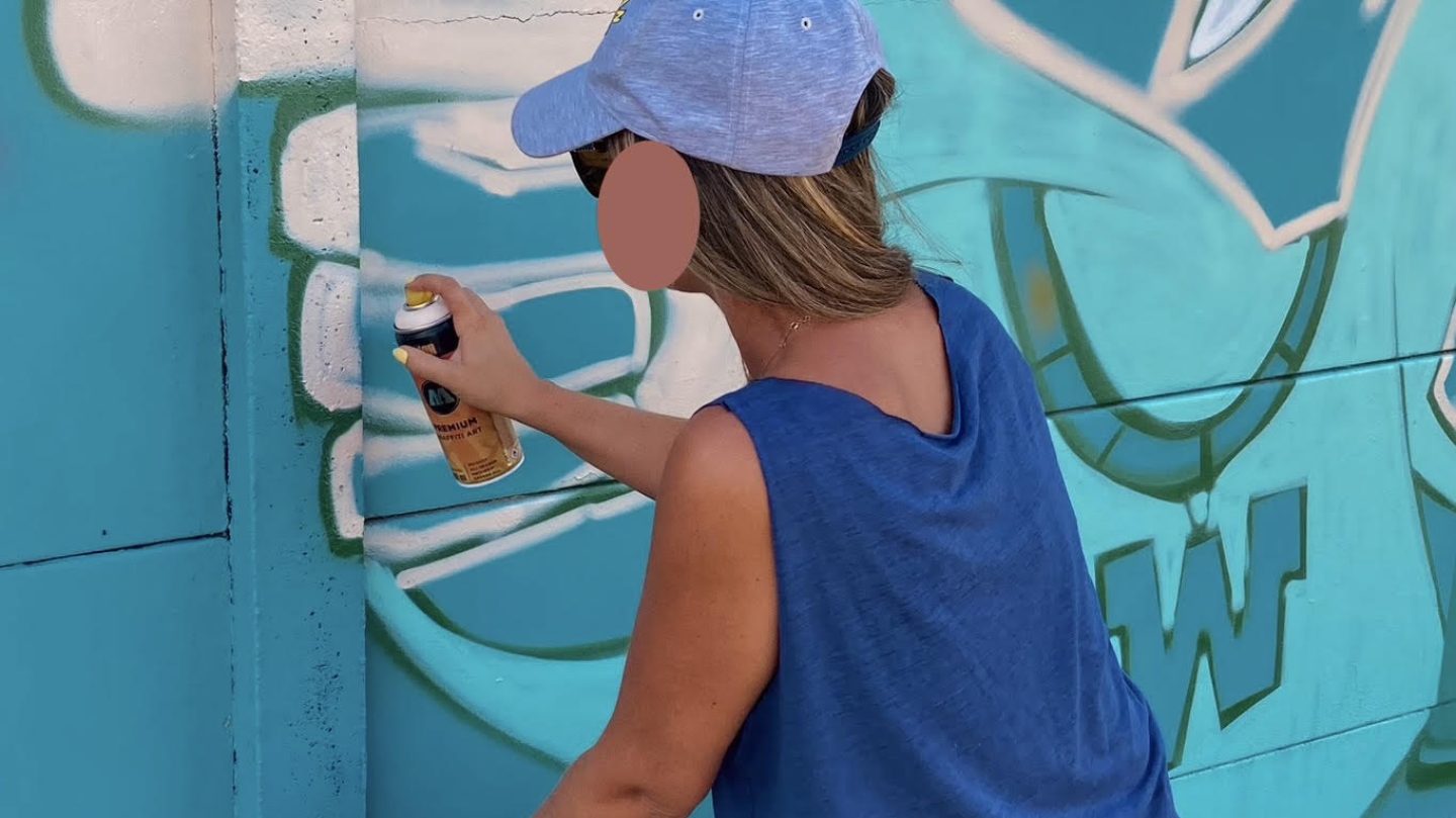 Participante peignant à la bombe les détails d'un personnage Bboy sur une fresque turquoise au stade Jean-Raymond Guyon.