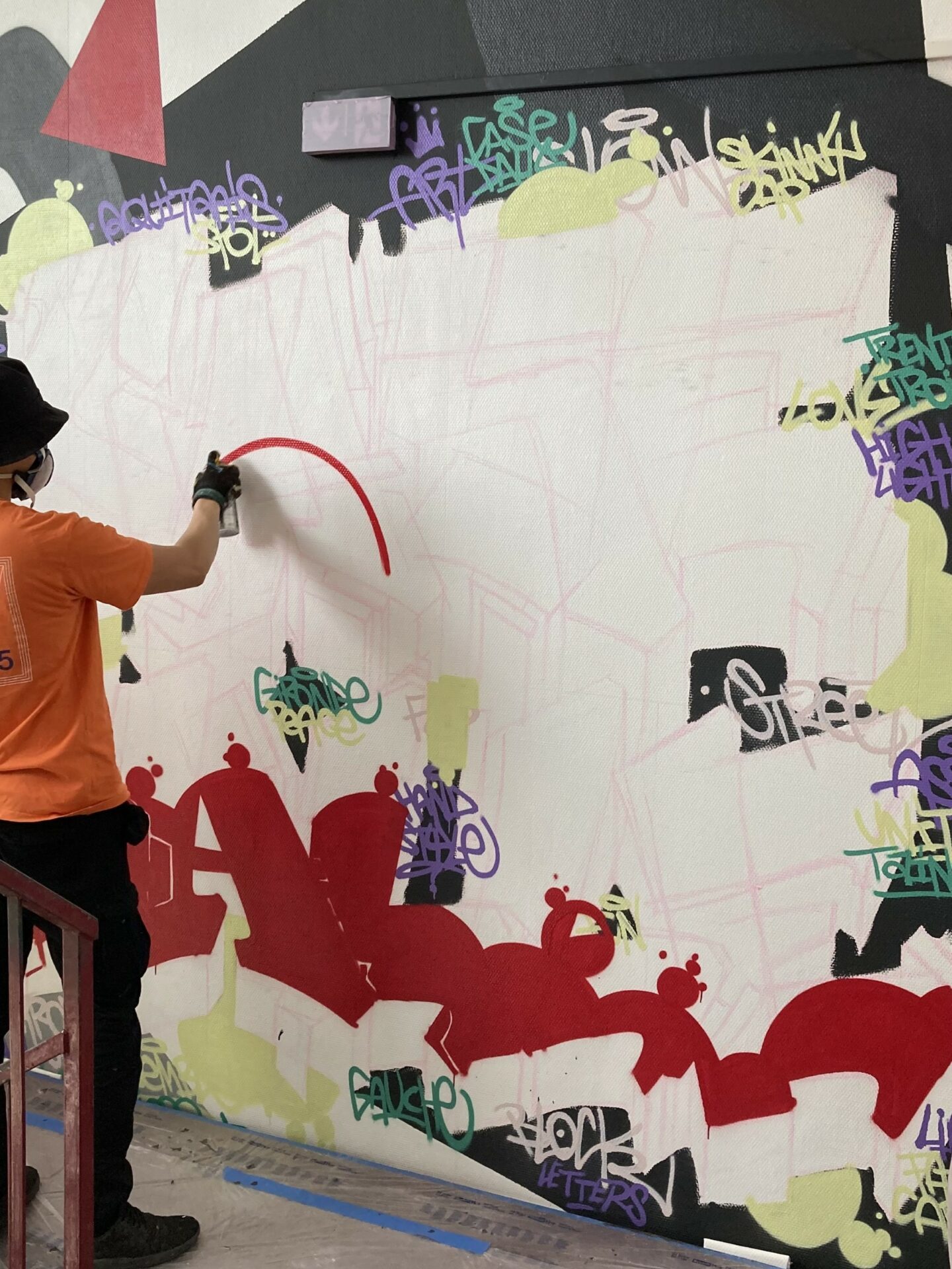 Artiste MEL20 réalisant un lettrage graffiti rouge à la bombe de peinture dans une cage d’escalier.