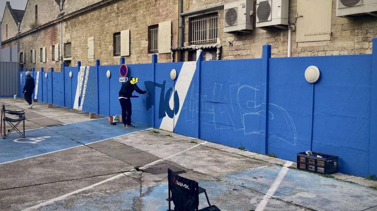 Préparation d’une fresque graffiti collaborative sur le parking Zolpan Bordeaux avec graffeurs peignant un long mur bleu lors d’un événement public au Cours du Médoc.