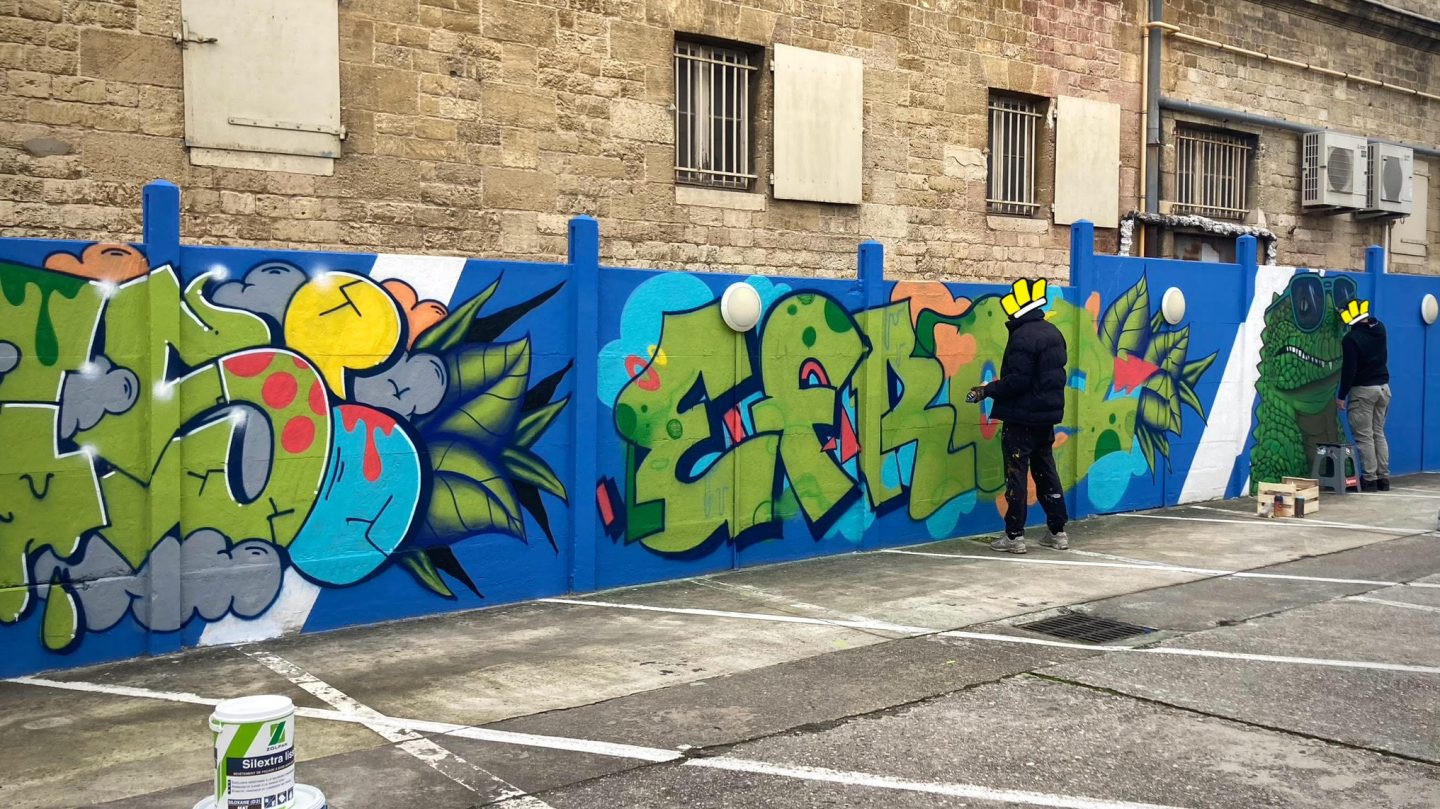Artistes graffiti travaillant sur une fresque murale colorée avec crocodile street art et lettrages urbains à Bordeaux.
