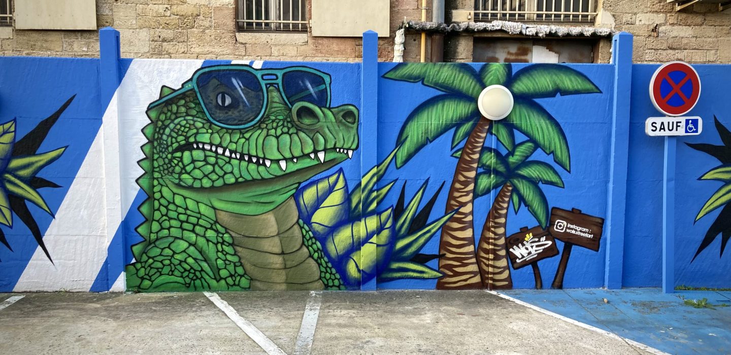 Crocodile graffiti avec lunettes de soleil et palmiers peint sur le mur bleu du parking Zolpan Bordeaux.