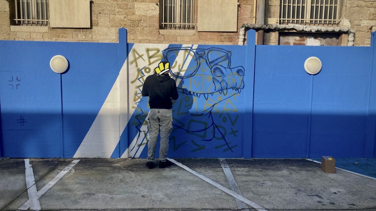 Artiste graffiti dessinant les premiers croquis d’une fresque sur mur bleu lors de l’événement artistique Zolpan Bordeaux au Cours du Médoc.