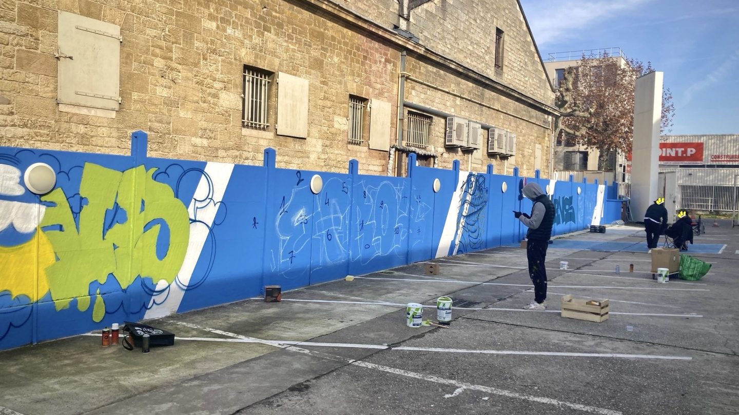 Progression d’une fresque graffiti urbaine sur un mur bleu du parking Zolpan Bordeaux pendant un événement street art public.