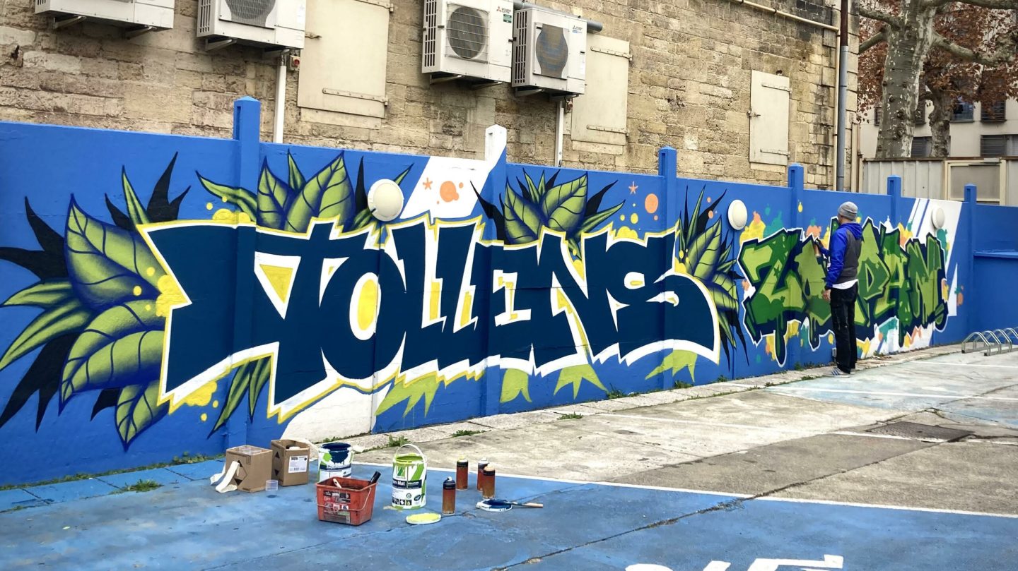 Lettrage graffiti TOLLENS peinte sur un mur bleu avec feuilles tropicales et style street art contemporain à Bordeaux.