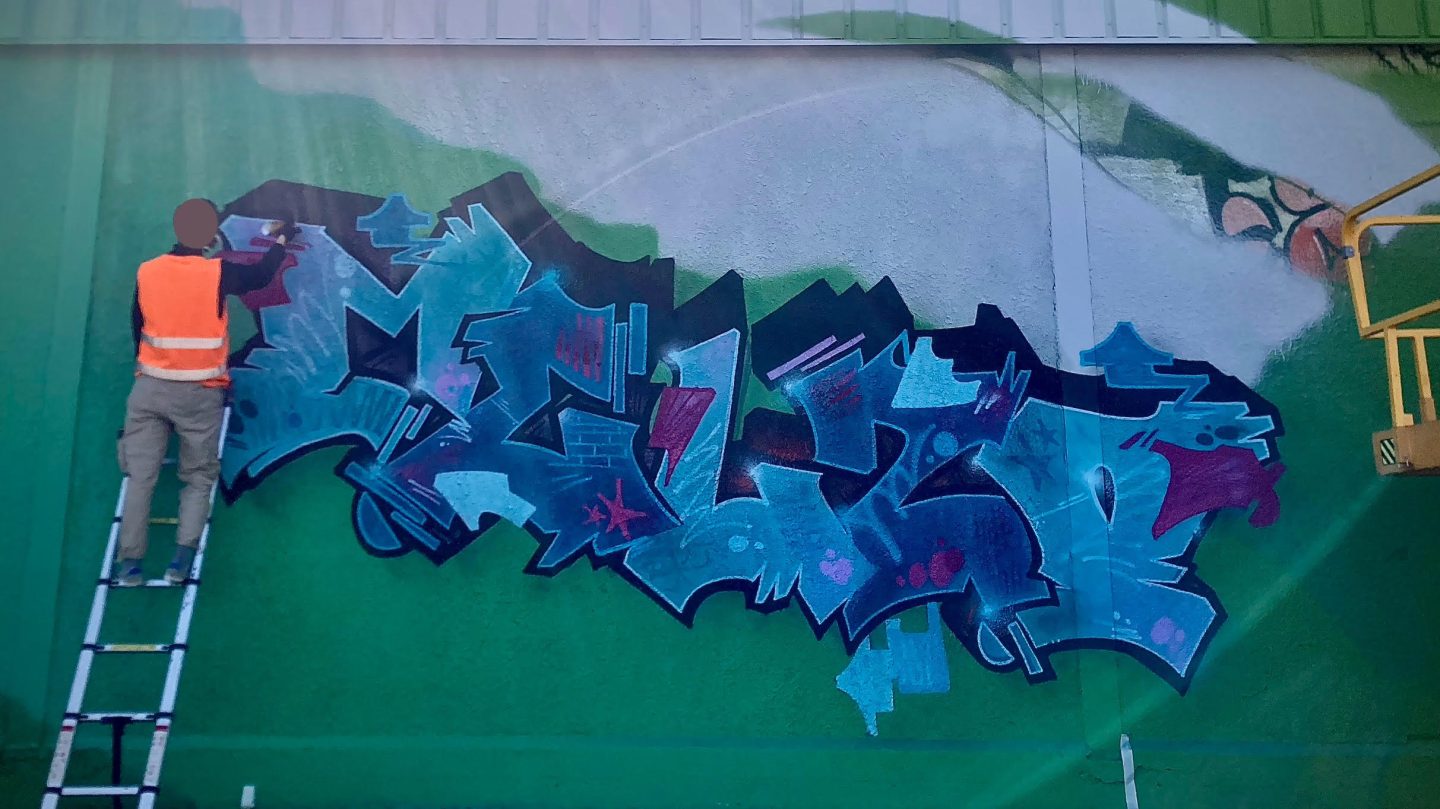 Artiste graffiti MEL20 réalisant un lettrage sur mur industriel