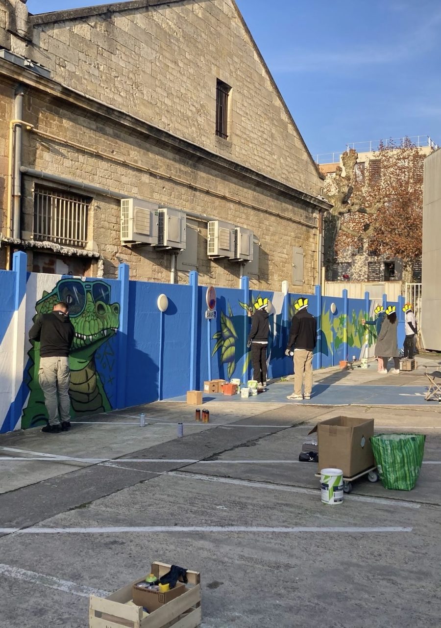 Artistes réalisant une fresque participative de graffiti sur un mur bleu lors d’un projet collaboratif avec Zolpan Bordeaux.
