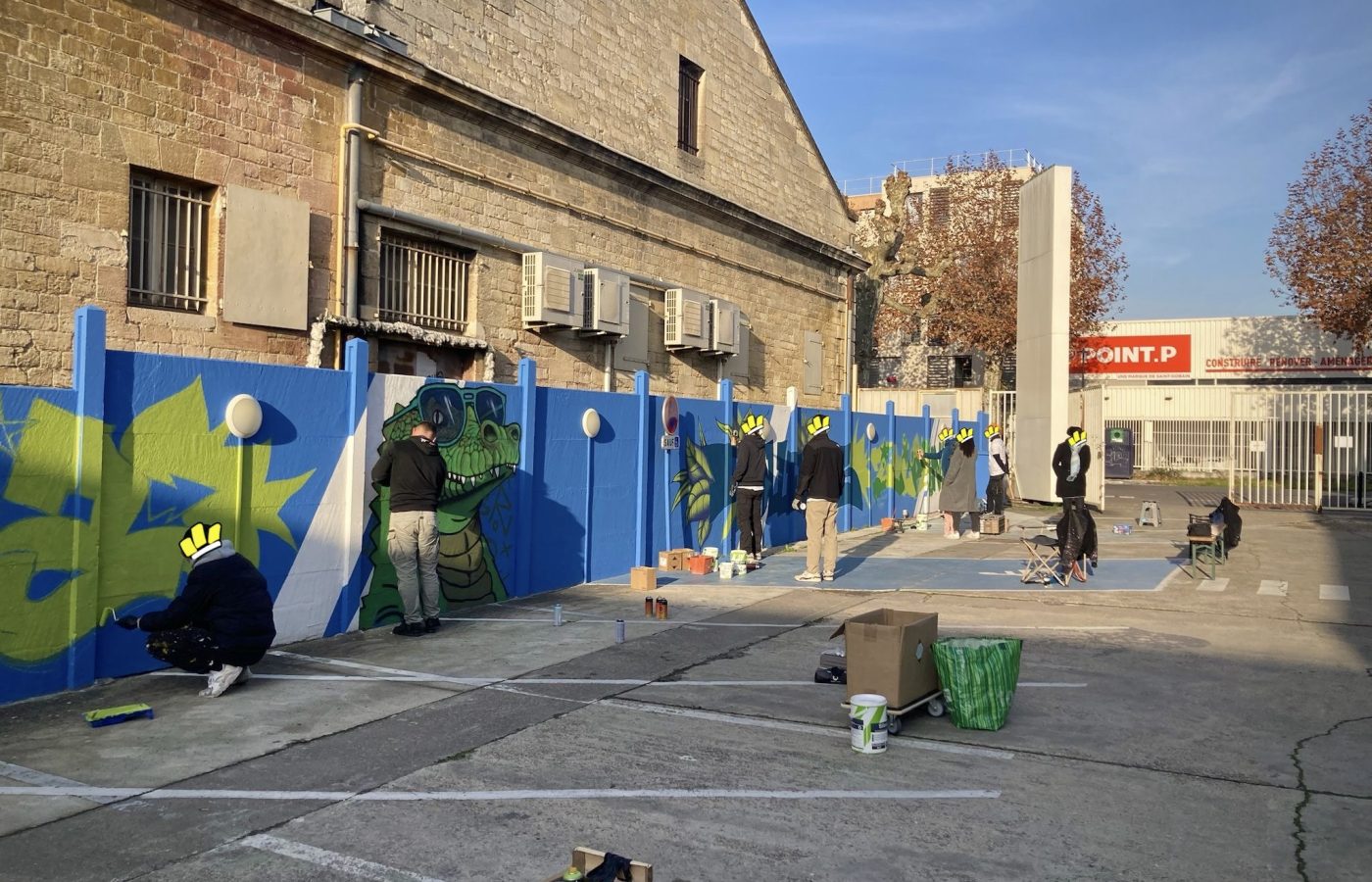 Artistes réalisant une fresque participative de graffiti sur un mur bleu lors d’un projet collaboratif avec Zolpan Bordeaux.