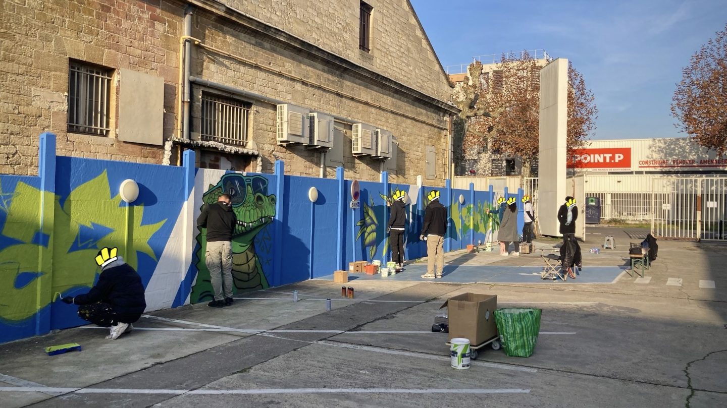 Artistes réalisant une fresque participative de graffiti sur un mur bleu lors d’un projet collaboratif avec Zolpan Bordeaux.