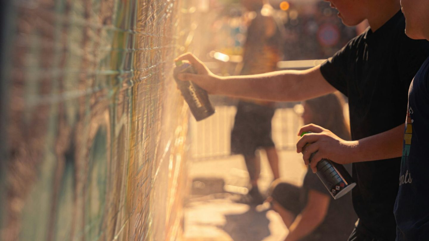 Initiation graffiti en extérieur avec adolescents réalisant une fresque street art à la bombe aérosol lors d’un atelier urbain.