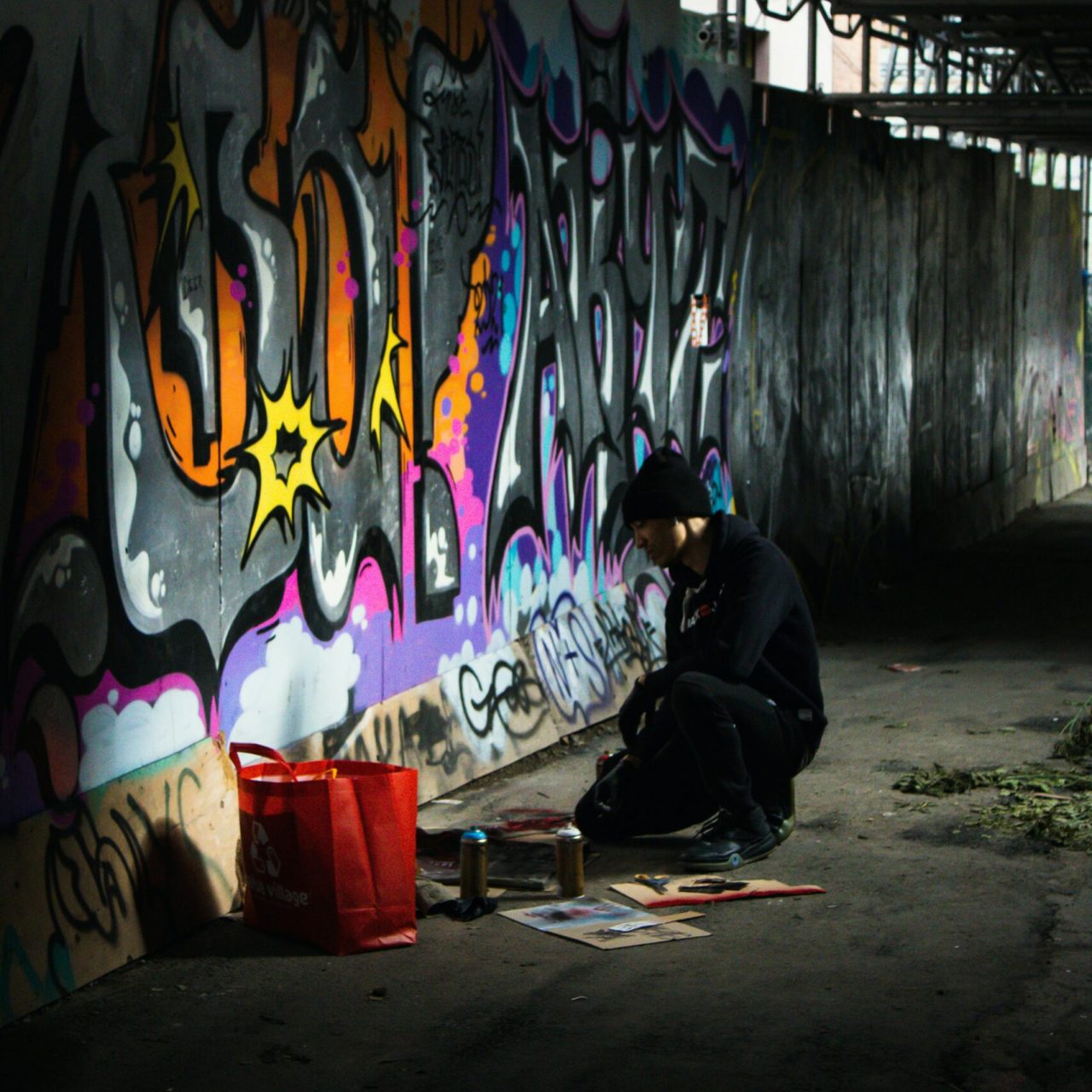 Artiste graffiti réalisant une fresque street art colorée dans un lieu urbain industriel avec bombes de peinture aérosol.