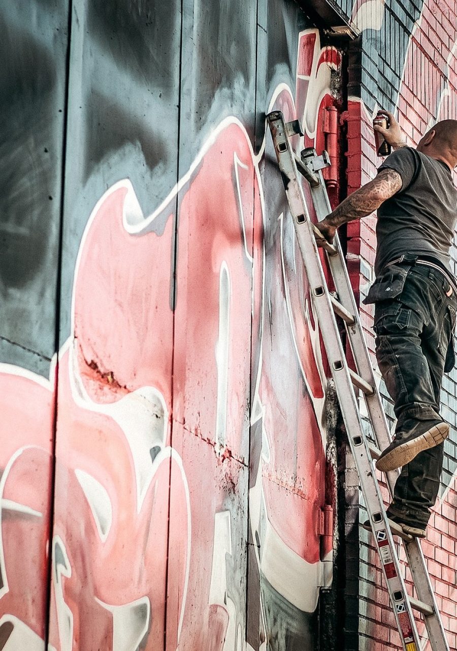 Artiste graffiti réalisant une fresque murale sur un bâtiment à l’aide d’une échelle