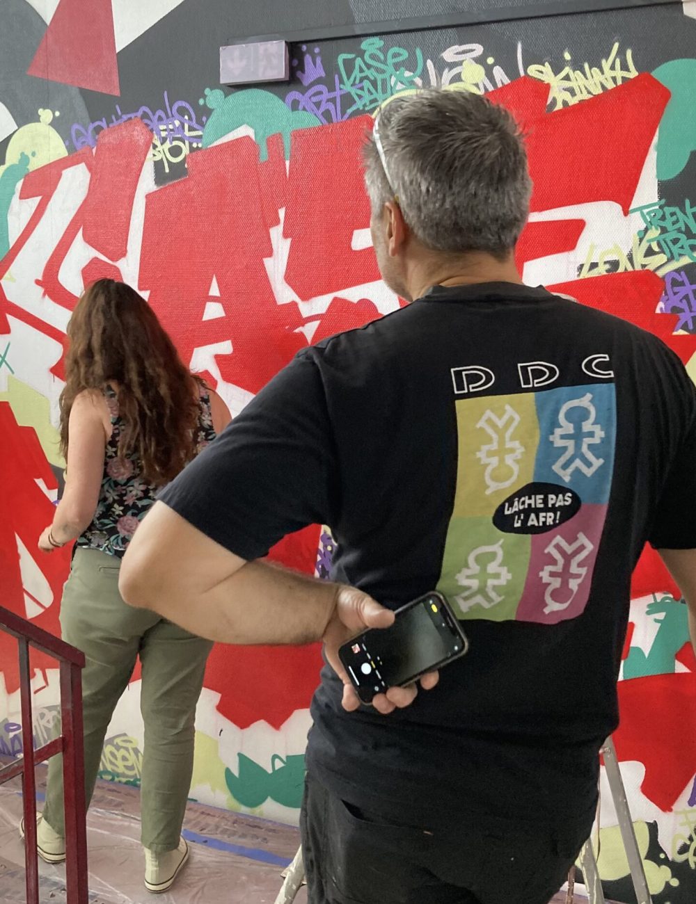 Participants observant la réalisation d’une fresque graffiti dans le cadre d’un chantier participatif à Bordeaux.
