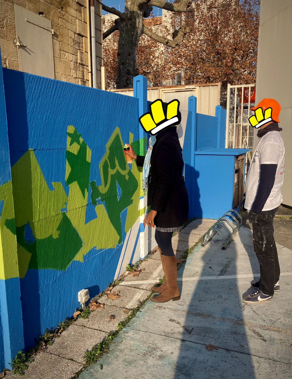 Participante initiée au graffiti peignant un lettrage vert sur mur bleu lors d’un atelier street art à Bordeaux.