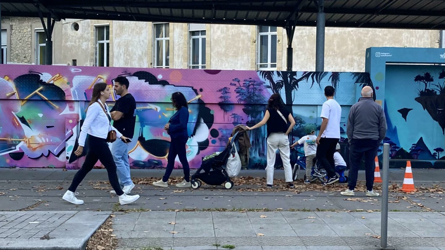 Passants marchant devant une fresque street art Avatar colorée dans un environnement urbain