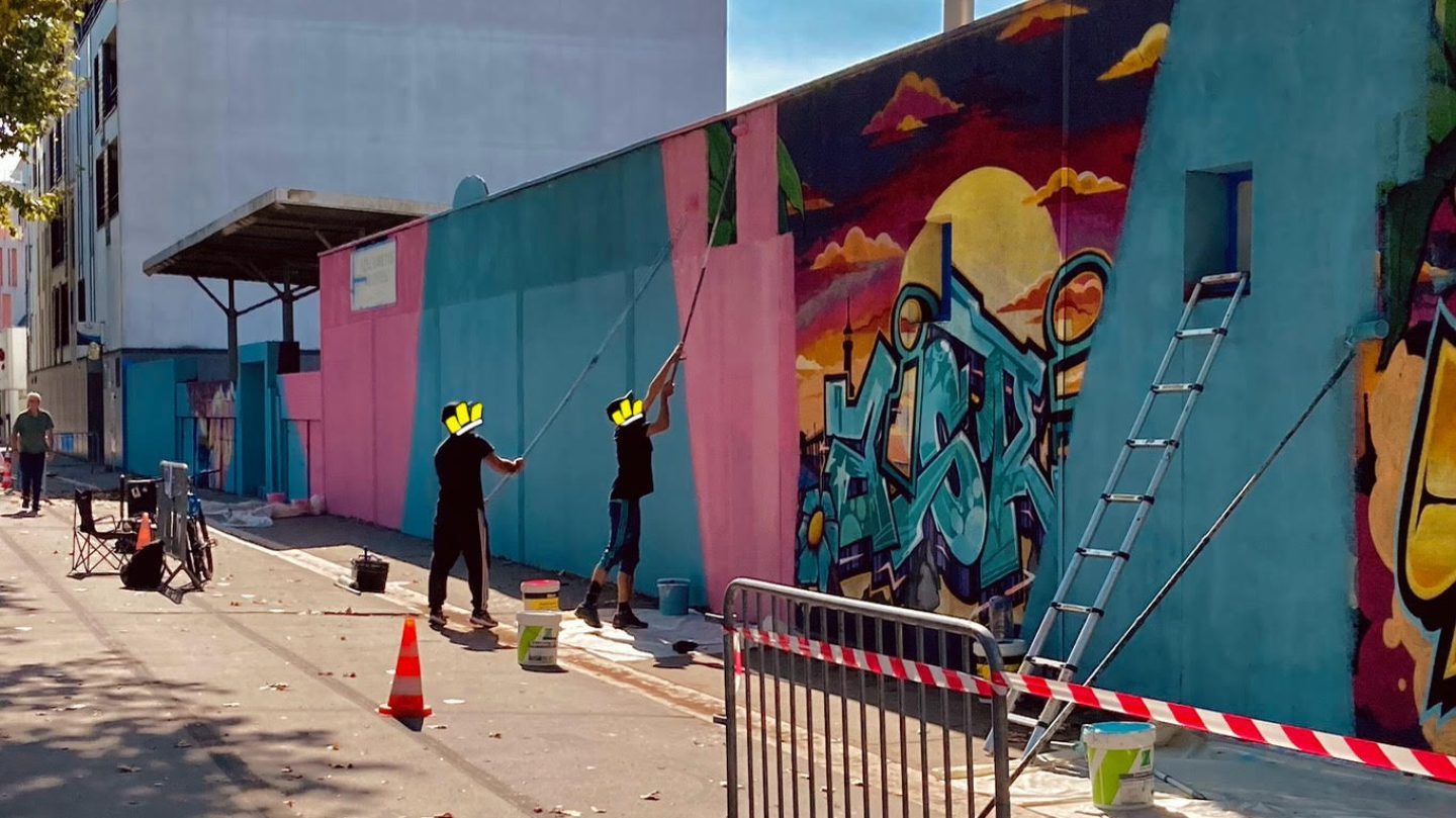 Vue d’ensemble d’un chantier de fresque murale avec artistes, matériel et mur en cours de transformation artistique