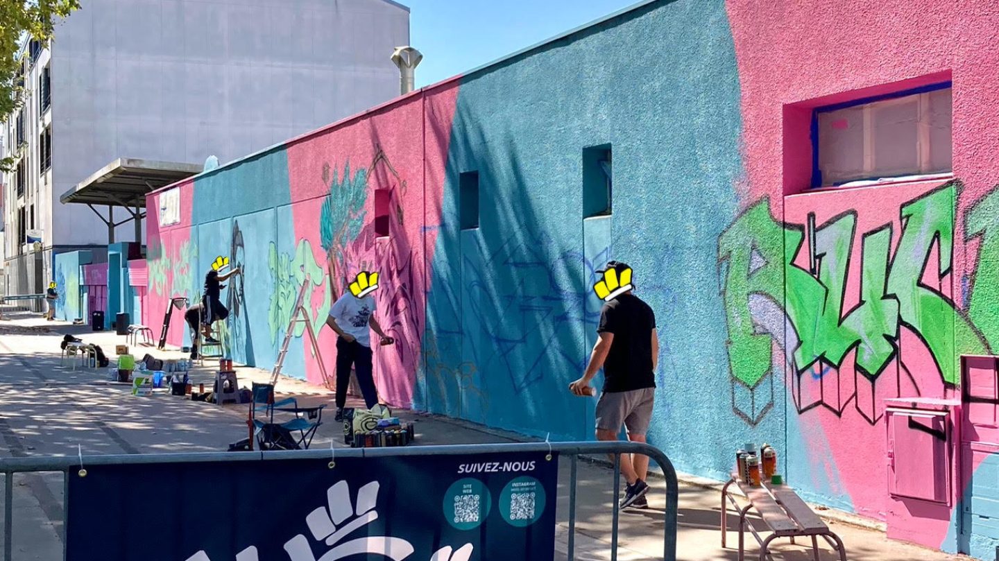 Artistes WOLS peignant une fresque murale colorée sur fond bleu et rose avec matériel de peinture et bombes de graffiti