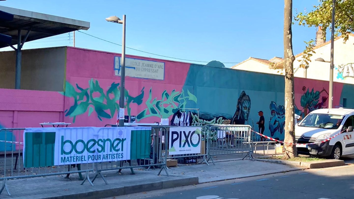Mur extérieur en cours de transformation artistique avec logos partenaires et fresque en progression lors d’un événement street art