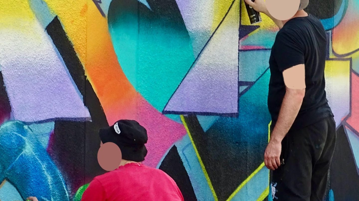 Deux artistes peignant une fresque graffiti colorée avec bombes de peinture sur un mur extérieur
