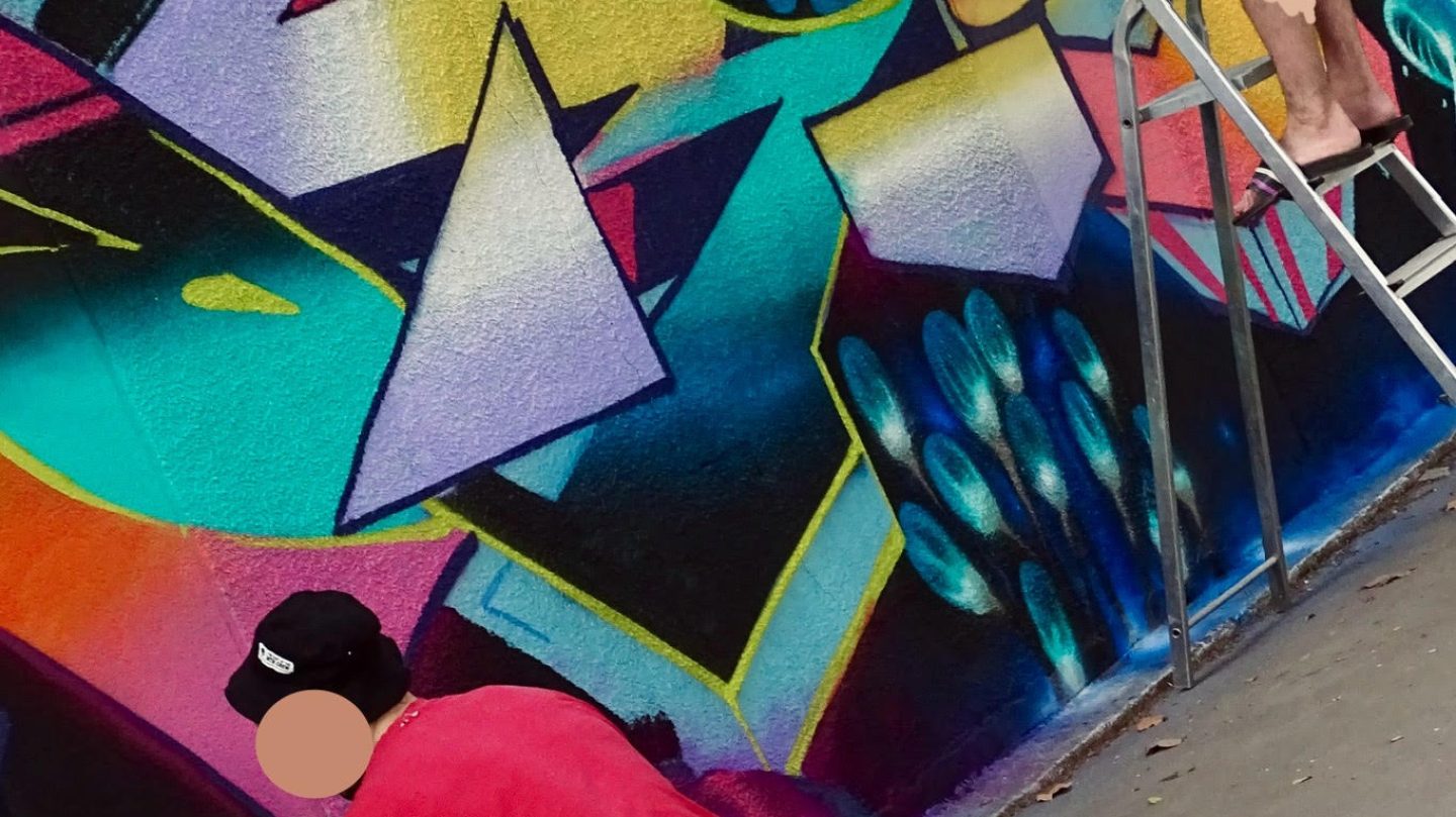 Artistes appliquant des dégradés et contours sur une fresque murale avec bombes de peinture