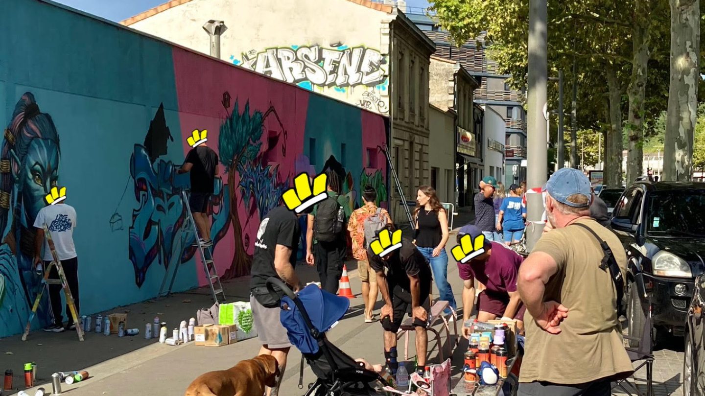 Vue d’ensemble d’un événement street art avec public, artistes et fresque murale en cours de réalisation