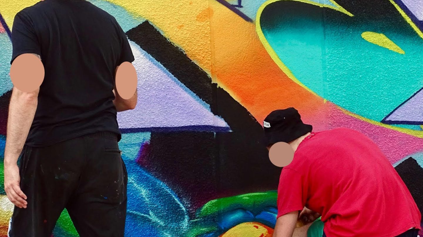 Artistes graffiti sélectionnant des bombes de peinture devant une fresque colorée en cours de réalisation